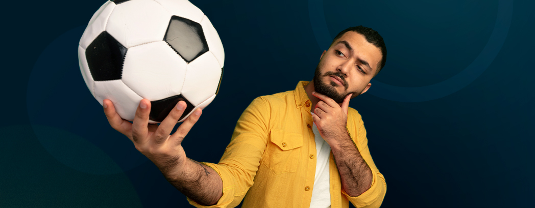 L'image montre un homme avec une main sur le menton et regardant son autre main qui tient un ballon de football.