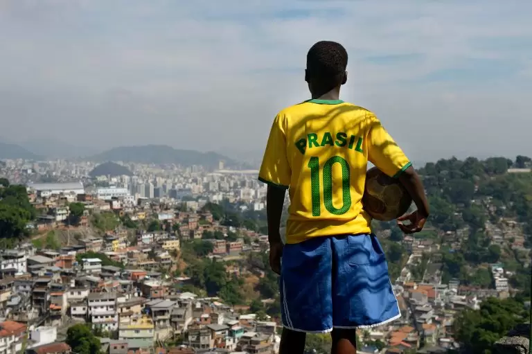 Menino com a camisa 10 da Seleção Brasileira segura uma bola de futebol