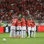 O grupo de jogadores do Internacional, vestidos com o tradicional uniforme vermelho de jogo, se abraçam em campo, no estádio Beira Rio.